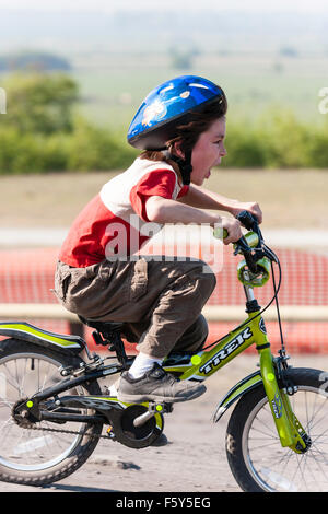 Seitenansicht der Kaukasischen 9 Jahre altes Kind, Junge, Reiten Fahrrad des Kindes bei der Geschwindigkeit mit aufgeregten Mimik. Trägt blaue Helm und T-Shirt. Stockfoto