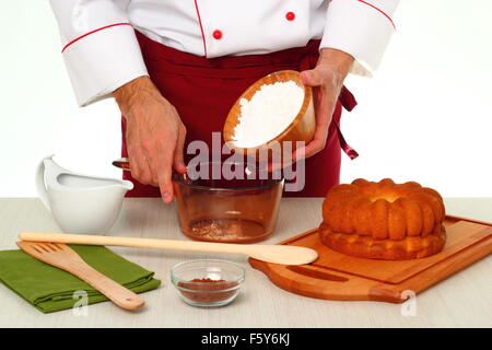 Hinzufügen von Puderzucker in Schüssel geben. Schokoladenglasur für Gugelhupf machen. Stockfoto