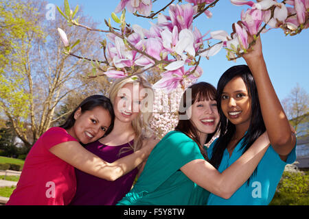 Vier glückliche junge Frauen stehen unter einem Magnolienbaum Stockfoto