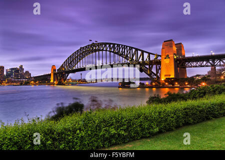 Seitenansicht der berühmten Sydney Harbour Bridge bei Sonnenuntergang mit Beleuchtung von grünen Erholungspark in Milsons Point mit Büschen Stockfoto