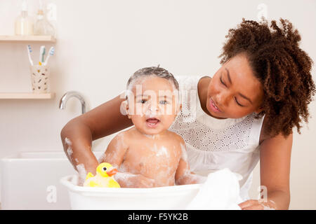 Kleiner Junge, ein Gesicht ziehen, während seine Mutter ihn Bäder Stockfoto