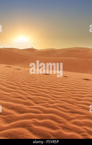 Wüstenlandschaft, Sonnenuntergang hinter Dünen, Menschen Silhouetten im Hintergrund und Fußspuren im sand Stockfoto