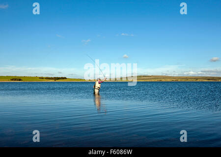 Fliegenfischen Sie auf Colliford Stausee Lake Bodmin Moor Cornwall einsamen Mann casting mit Stab auf noch See blauer Himmel Stockfoto