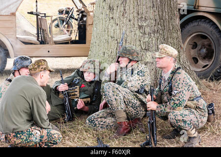 Weltkrieg zwei Re-enactment. Gruppe deutscher Soldaten unter dem Baum sitzen, Plaudern und Entspannen. Zwei von ihnen in der Tarnung Kittel. Stockfoto