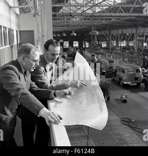 Geschichtsbild der 1950er Jahre, zwei Führungskräfte oder Manager der British Motor Corporation oder BMC studieren Fertigungsplänen oder Diagramme, mit Blick auf den van-Produktionsstraße. Stockfoto