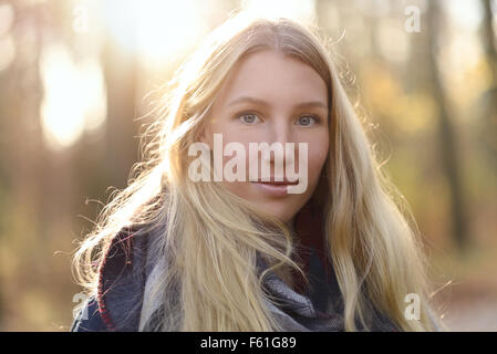 Attraktive junge Frau mit langen blonden Haaren im Herbst Mode tragen einen trendigen Schal stehen im Freien im Herbst Wald lächelnd Stockfoto