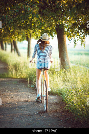Schöne junge Frau mit Hut mit dem Fahrrad in einem Park - Blick von der Rückseite Stockfoto