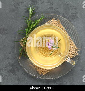 Frisch zubereitete Rosmarin Kräutertee in Glasschale, garniert mit Rosmarin Blume, fotografiert overhead auf Schiefer Stockfoto