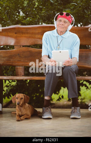 Älterer Mann mit Kopftuch, Sonnenbrillen und Kopfhörer, hören Rock'n'Roll auf dem Tablet. Stockfoto