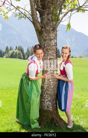 Zwei lächelnde Frauen im Dirndl festhalten an einem Baum. Stockfoto