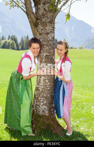 Zwei lächelnde Frauen im Dirndl festhalten an einem Baum. Stockfoto