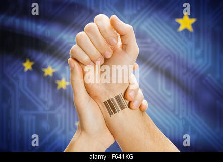 Barcode-ID Nummer Tatoo am Handgelenk und USA Statesl Flagge auf Hintergrund - Alaska Stockfoto