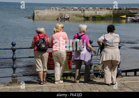 Sonnigen Sommertag & eine Gruppe von 4 Reifen Freundinnen im Urlaub, stehend, mit Blick auf das ruhige Meer & Harbour, Staithes, Yorkshire, England, UK. Stockfoto