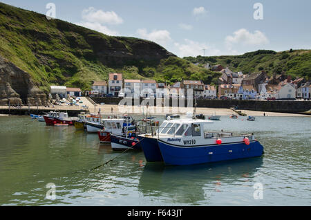 An einem sonnigen Sommertag sind bunte Fischerboote im Hafen von Meer, mit dem malerischen Dorf Staithes, North Yorkshire, UK, über festgemacht. Stockfoto