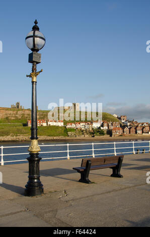 Einen sonnigen Abend Blick auf einen Laternenpfahl und leere Bank auf der West Pier in Whitby, North Yorkshire - die Abtei und die Kirche über. Stockfoto