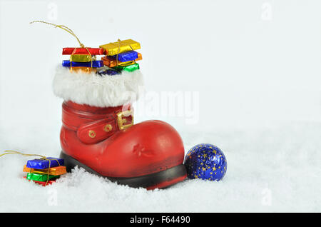 Nahaufnahme von einem roten Boot mit weißem Fell Trimmen, gefüllt mit Süßigkeiten, auf weißen, schneebedeckten Hintergrund, horizontale Stockfoto