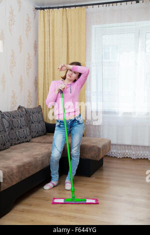 müde Mädchen in eine rosa Bluse und blaue Jeans waschen Holzboden mit einem Mopp Stockfoto