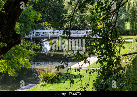 Weißen hölzernen Brücke über einen kleinen Fluss mit überhängenden Bäumen. Stockfoto