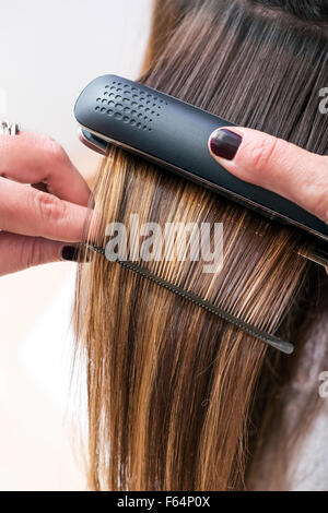 Friseur Begradigung der langen braunen Haaren eines weiblichen Kunden mit einem beheizten Haarglätter Nahaufnahme ihrer Hände Stockfoto