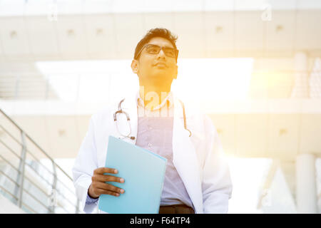 Asiatischen indischen Arzt außerhalb Klinikgebäude, schönen goldenen Sonnenlicht im Hintergrund stehen. Stockfoto