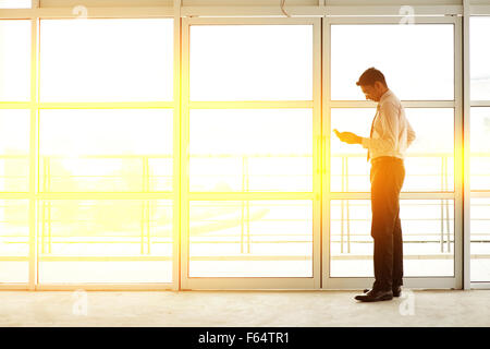 Asiatische indische Geschäftsmann mit Handy im modernen Büro Gebäude, goldenen Sonnenuntergang Hintergrund. Stockfoto