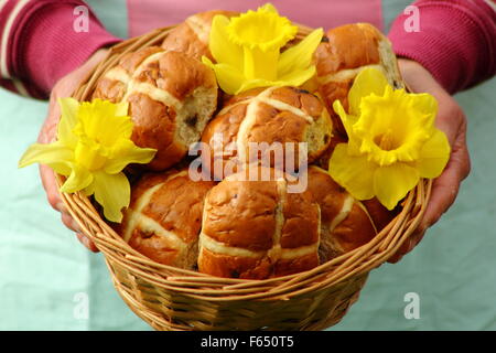 Eine Frau stellt Hot Cross Buns dekoriert mit Narzissen in einem rustikalen Weidenkorb für die Osterfeiertage in Nord-England, UK Stockfoto