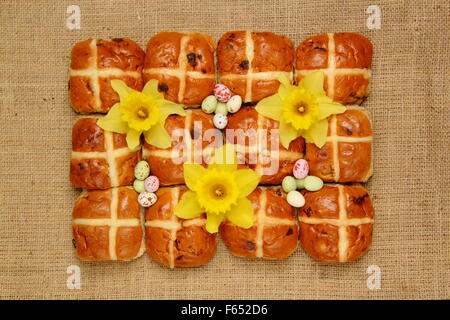 Hot Cross Buns dekoriert mit Narzissen und Schokoladeneier zu Ostern vor dem Hessischen Hintergrund, England UK Stockfoto