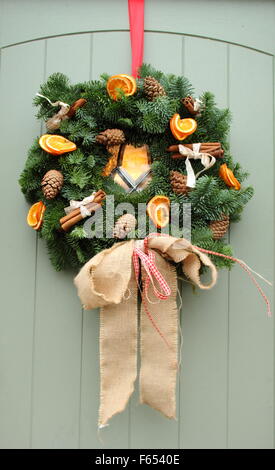 Ein Weihnachtsgirlande oder Kranz, mit Zimt-sticks und getrocknete Orangenscheiben hängt an einer Hütte Tür in England, UK Stockfoto