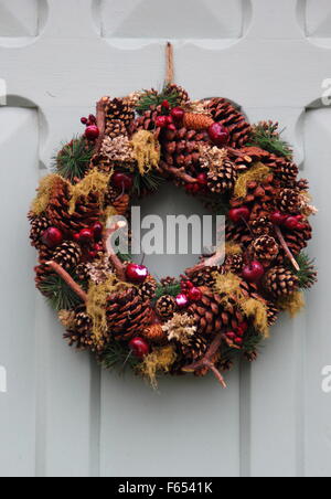 Eine Weihnachtsgirlande oder Kranz, hergestellt mit Zapfen, Moos und faux Obst hängt an einer Tür aus Holz Land in der Peak District UK Stockfoto