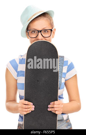 Vertikale Schuss von einem blonden Hipster Mädchen durchlöchern eine Skateboard vor ihr Gesicht und spähen hinter es Stockfoto
