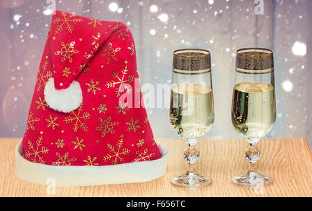 Auf dem Tisch neben dem Fenster Stand zwei schöne Gläser gefüllt mit Champagner und Hut von Santa Claus. Weihnachten, schneit. Stockfoto