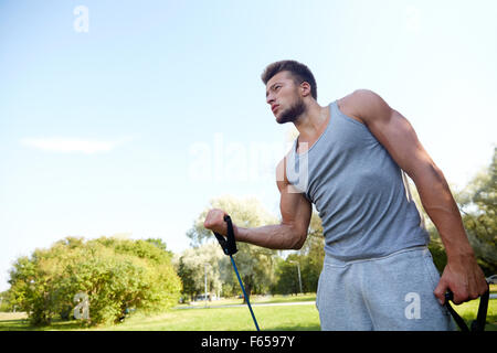 junger Mann mit Expander im Sommerpark Ausübung Stockfoto
