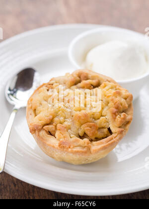 Kleine Runde Apfelkuchen auf einem weißen Teller mit einer Kugel Vanilleeis serviert. Stockfoto