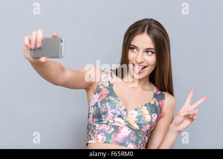 Schöne junge glücklich selbstbewusste Frau in floral Top Selfie machen und Zunge zeigen Stockfoto