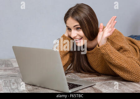 Fröhliches aufgeregt Mädchen, video-Konferenz junge Frau auf dem Boden mit laptop Stockfoto
