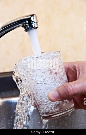 Wasser fließt aus einem Hahn in ein Glas. Stockfoto