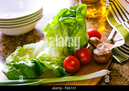 Kopfsalat, Tomaten und Frühlingszwiebeln, Bambus Schneidbrett, Tuch und Öl auf Granit Arbeitsplatte, Hinterleuchtung Stockfoto