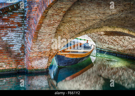 Schmutzige Boot und historischen Brücke von Comacchio, Stadt, bekannt als The Little Venice in Emilia-Romagna, einer bezaubernden Lagunenstadt mit Brücken und Kanälen durchzogen Stockfoto