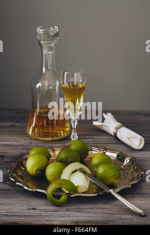 Limoncello in einem klassischen eleganten Flasche und Glas mit grüner Zitrone auf einem silbernen Teller mit einem Messer Stockfoto