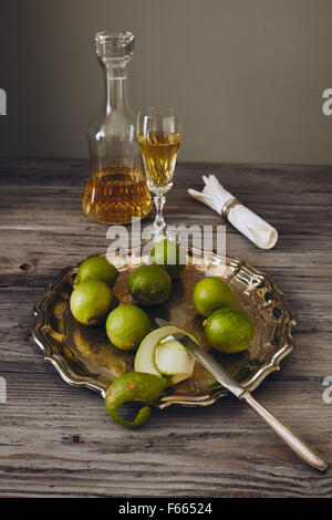 Limoncello in einem klassischen eleganten Flasche und Glas mit grüner Zitrone auf einem silbernen Teller mit einem Messer Stockfoto