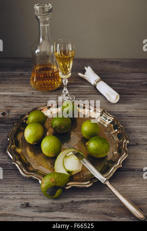 Limoncello in einem klassischen eleganten Flasche und Glas mit grüner Zitrone auf einem silbernen Teller mit einem Messer Stockfoto