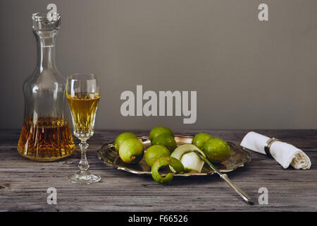 Limoncello in einem klassischen eleganten Flasche und Glas mit grüner Zitrone auf einem silbernen Teller mit einem Messer Stockfoto