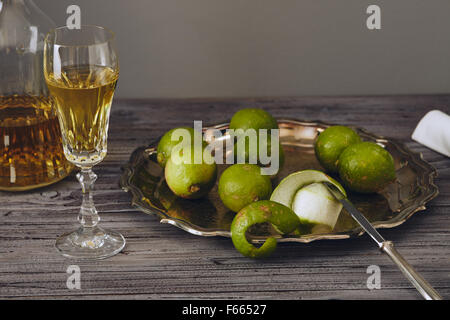 Limoncello in einem klassischen eleganten Flasche und Glas mit grüner Zitrone auf einem silbernen Teller mit einem Messer Stockfoto