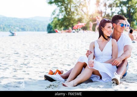 Romantische junges Paar in Liebe sitzen an einem Sandstrand und lächelnd Stockfoto