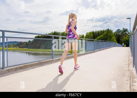 Schlanke Frau läuft im Freien auf Brücke über einem See Stockfoto