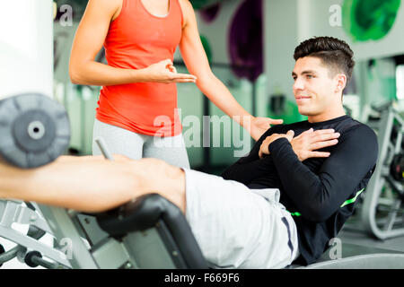 Schöne junge Frau, einen jungen Mann in der Turnhalle anweist und mit Blick auf sein Training Stockfoto