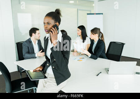 Schöne, junge, schwarze Geschäftsfrau hält eine Tablette in einem Büro treffen und schlechte Nachrichten auf dem Handy macht ihre co Stockfoto