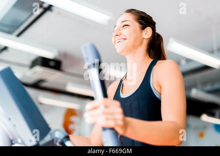 Schöne junge Dame mit dem elliptischen Trainer in einem Fitnessstudio in eine positive Stimmung Stockfoto