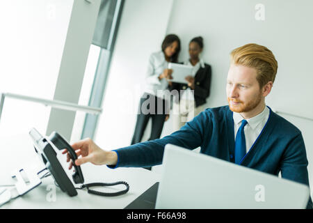 Geschäftsmann zu beantworten das Telefon mit zwei schöne, junge Frauen, die ein Gespräch im Hintergrund Stockfoto