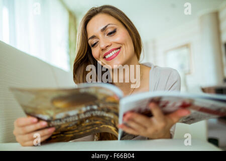 Schöne Frau auf einem Sofa ein Papier in einem gut beleuchteten stilvolle Wohnzimmer lesen Stockfoto